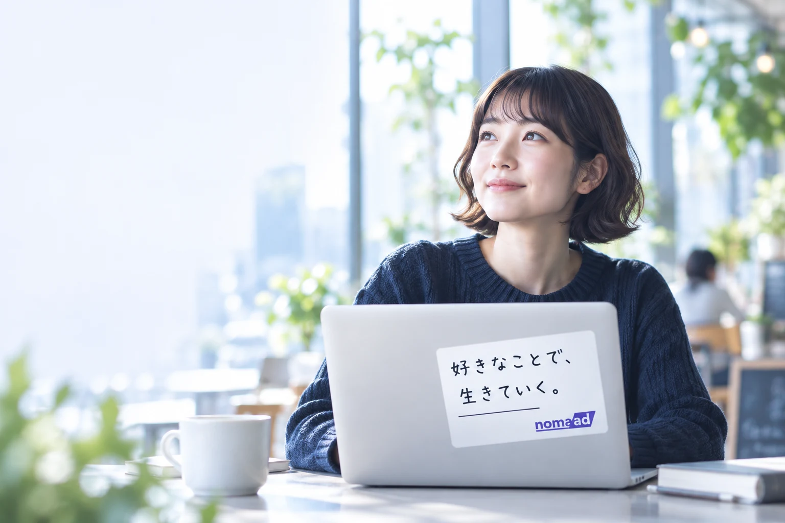 自然光の入るカフェで、nomaadステッカーを貼ったノートPCを使う女性のイメージ